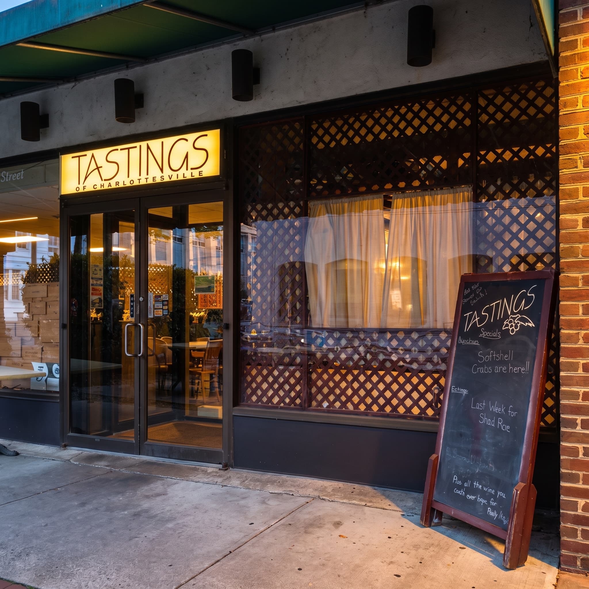 The Tastings storefront at dusk, sign glowing, sidewalk chalkboard out